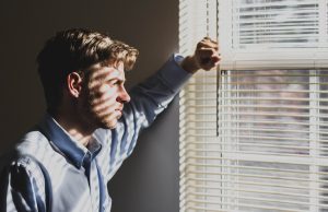 Man looking out through slatted blinds